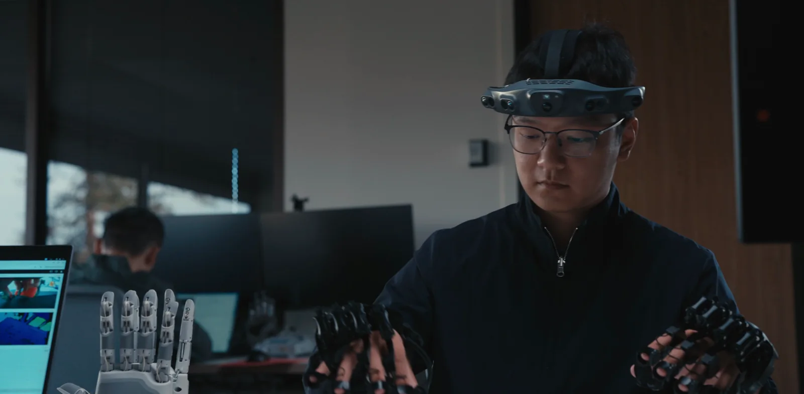 An engineer wearing a head camera and two Aero UMIs, with Aero Hands on the desk.